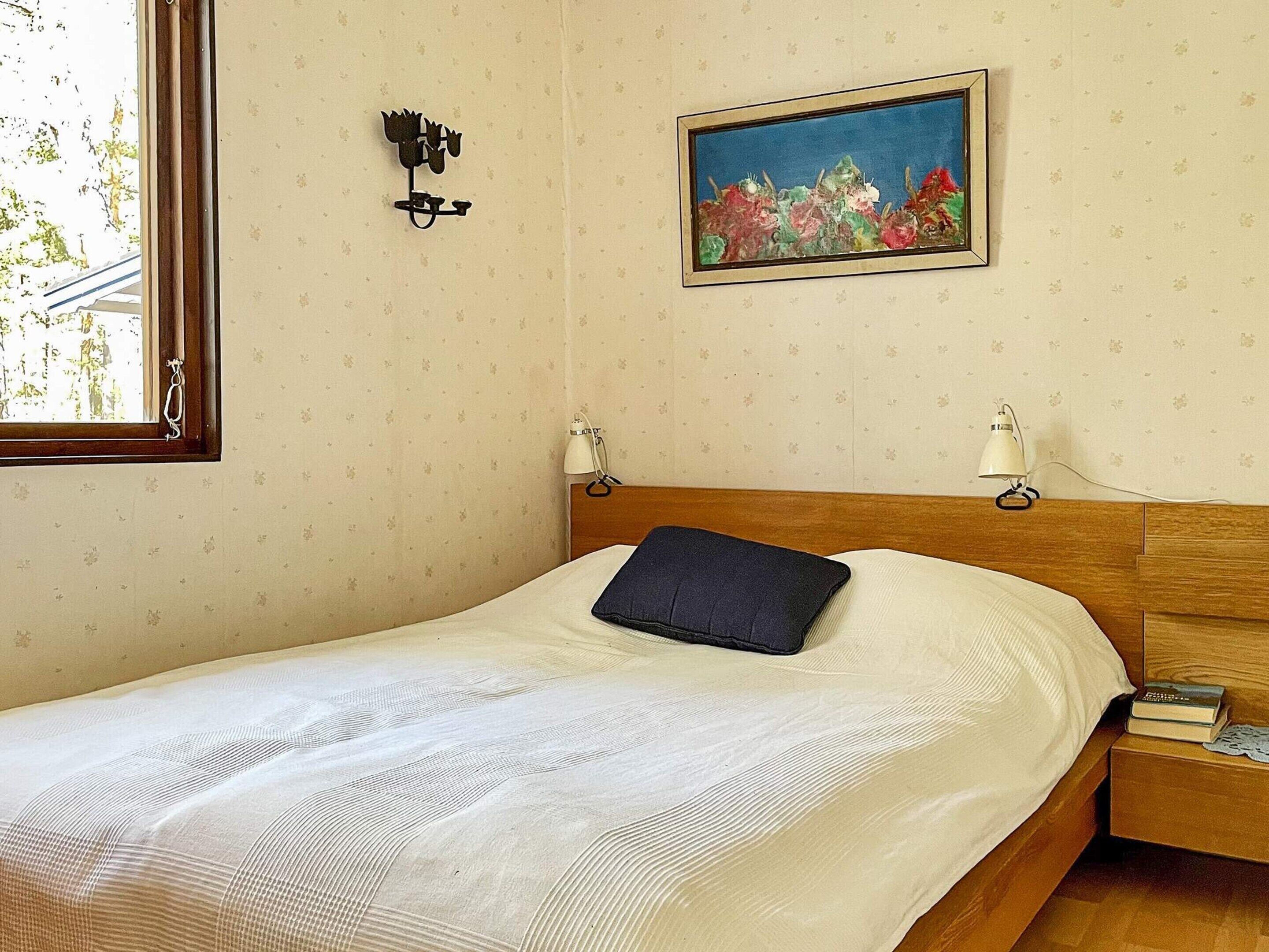 A neatly made bed with a dark pillow, a wall-mounted picture, and two bedside lamps.