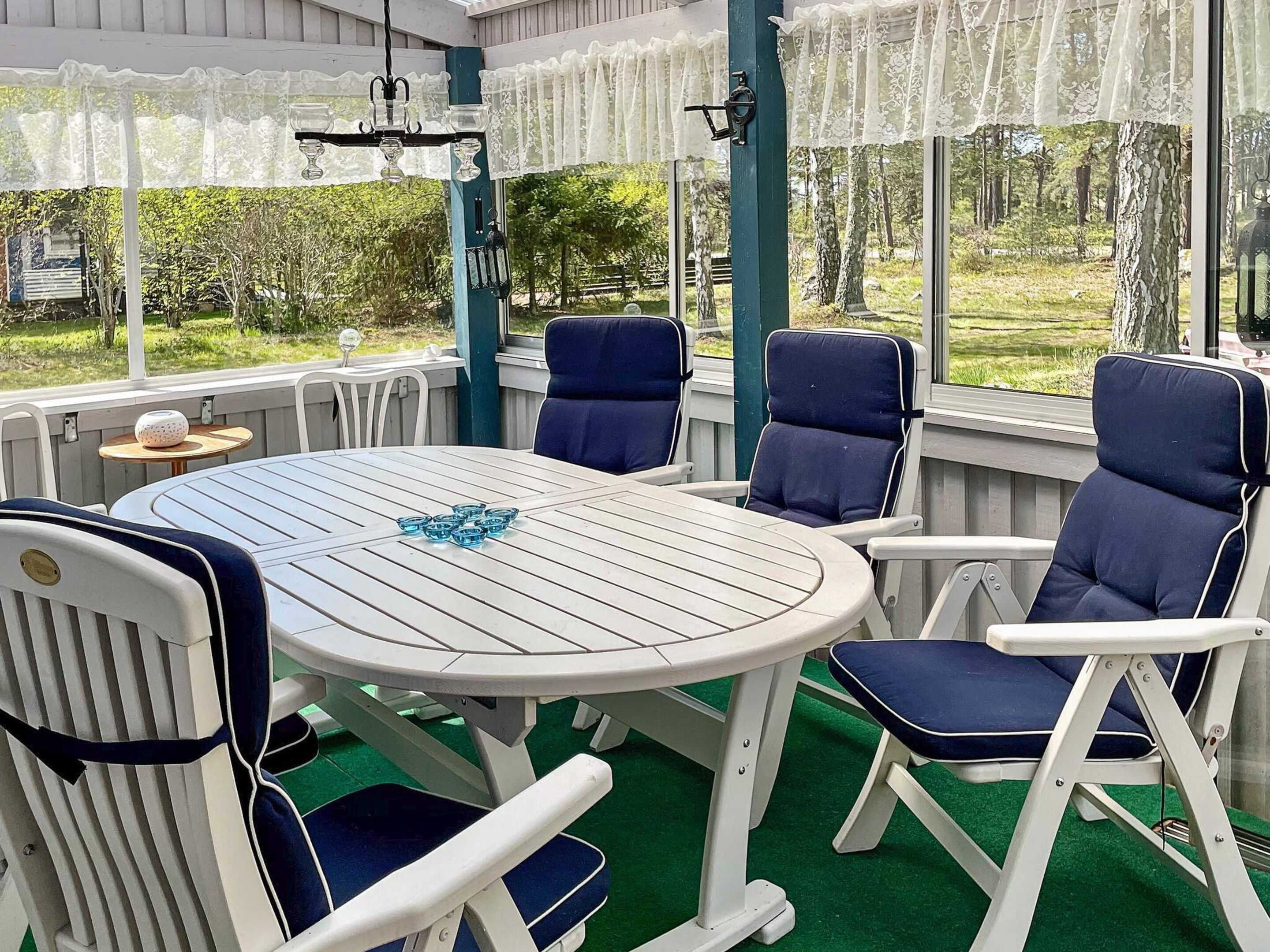 A covered outdoor seating area with a round table and chairs, a decorative hanging light fixture, and a view of greenery outside.