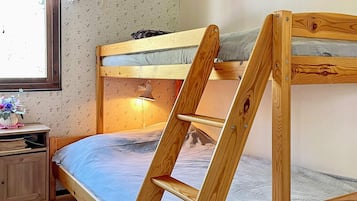 A bunk bed with a wooden ladder, a bedside lamp, and a small wooden nightstand with a vase of flowers.