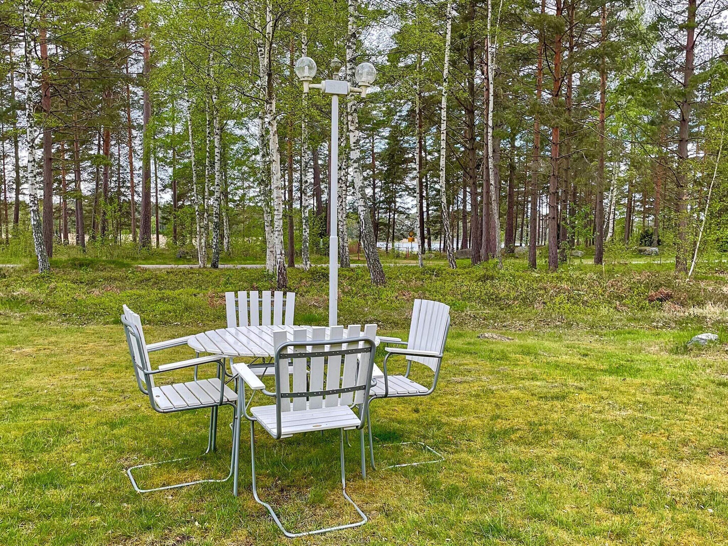 Une table de pique-nique avec des chaises, installée dans un espace herbeux entouré d’arbres.