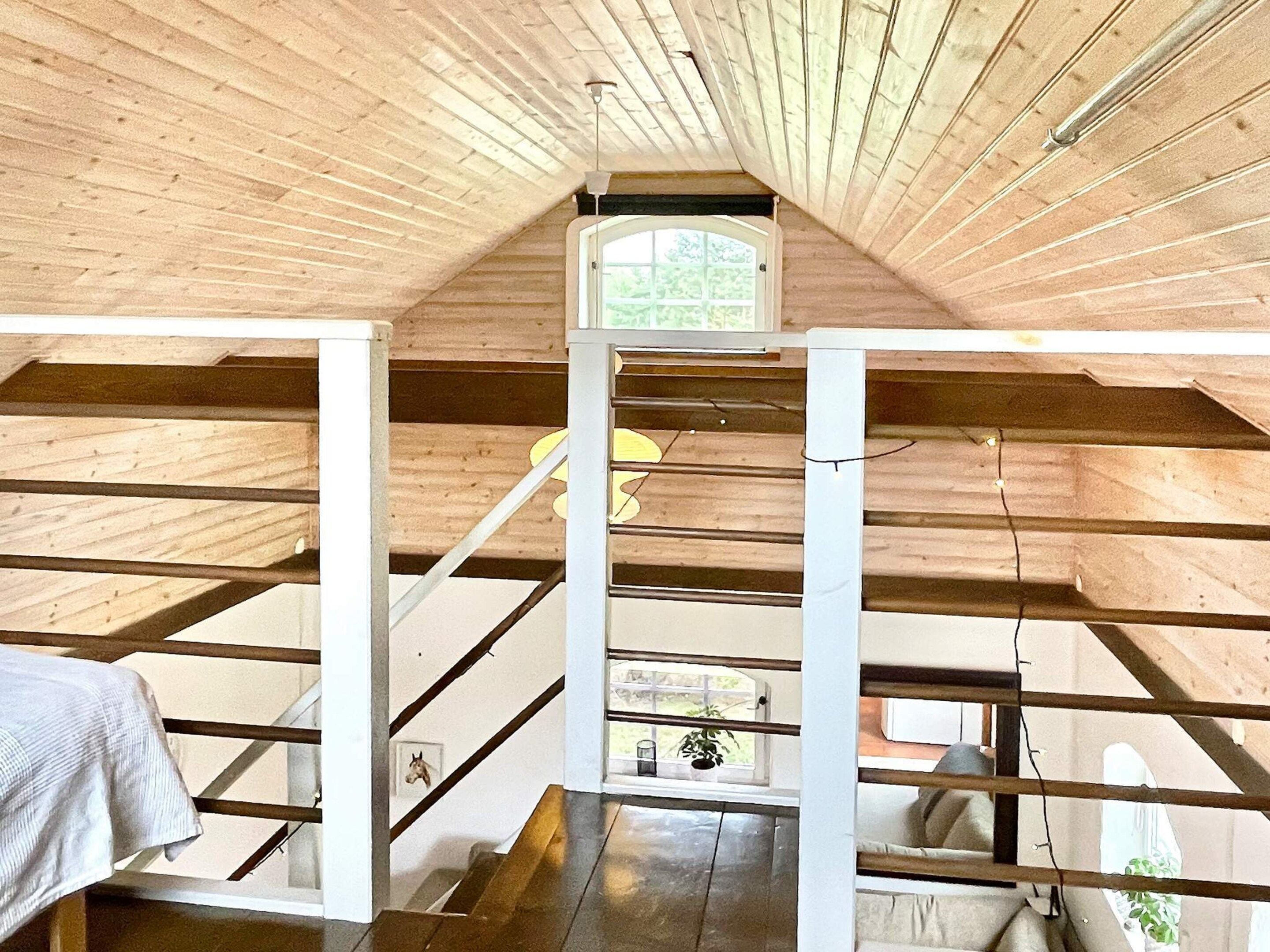Un dormitorio en el ático con vigas de madera, un tragaluz y una escalera.
