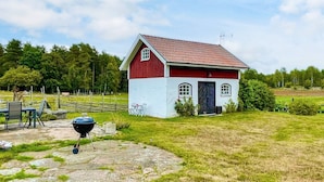 Una casita pequeña de color rojo y blanco con techo rojo, una parrilla negra y un patio de piedra.