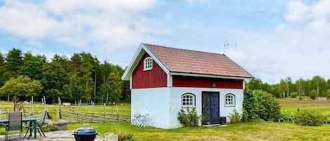 Una casita pequeña de color rojo y blanco con techo rojo, una parrilla negra y un patio de piedra.