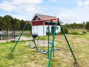 A white house with a red roof, a swing set, and a grill in the yard. - 3 Person Holiday Home in Berga (Berga)
