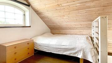 A small, sloped-roofed room with a single bed, a wooden dresser, and a window.