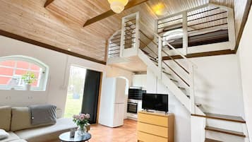 A spacious living area with a wooden ceiling, a staircase, a sofa, a dining table, and a TV.