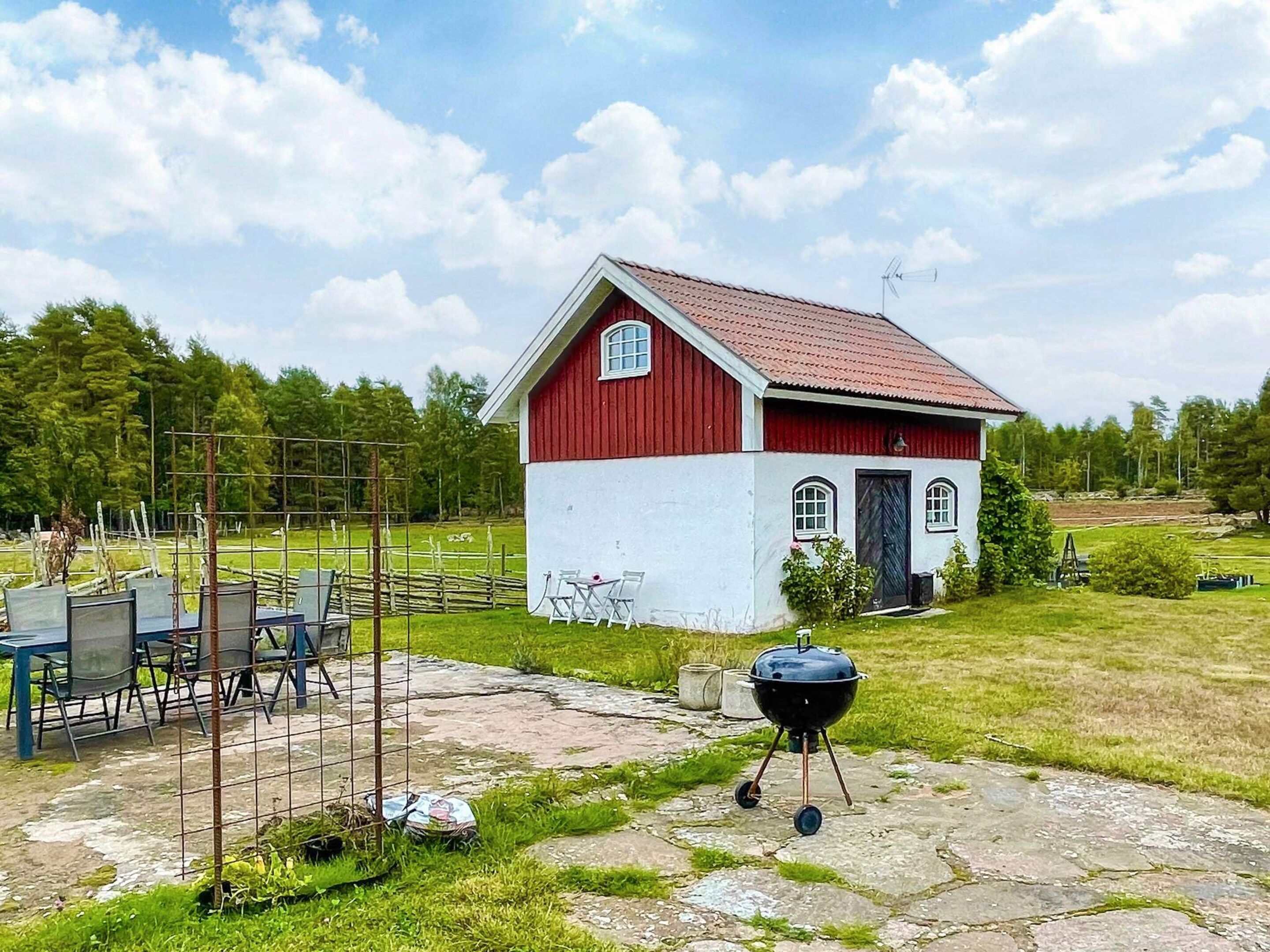 Ein rotes und weißes Bauernhaus mit einem Metallgitter und Stühlen im Vordergrund.