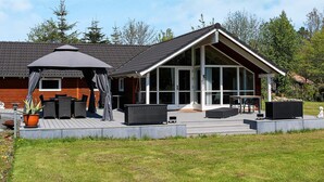 Et moderne hus med en overdækket terrasse, udendørs møbler og et stort vindue med udsigt over en græsplæne.
