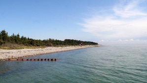 A beach with a clear sky, calm water, and a forested area in the background. - 8 Person Holiday Home in Hadsund (Hadsund)