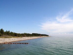 A beach with a clear sky, calm water, and a forested area in the background. - 8 Person Holiday Home in Hadsund (Hadsund)