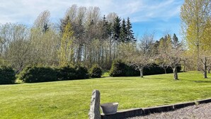 A well-maintained grassy area with a stone bench and a metal bucket, surrounded by trees and a clear sky. - 4 Star Holiday Home in Granna (Gränna)