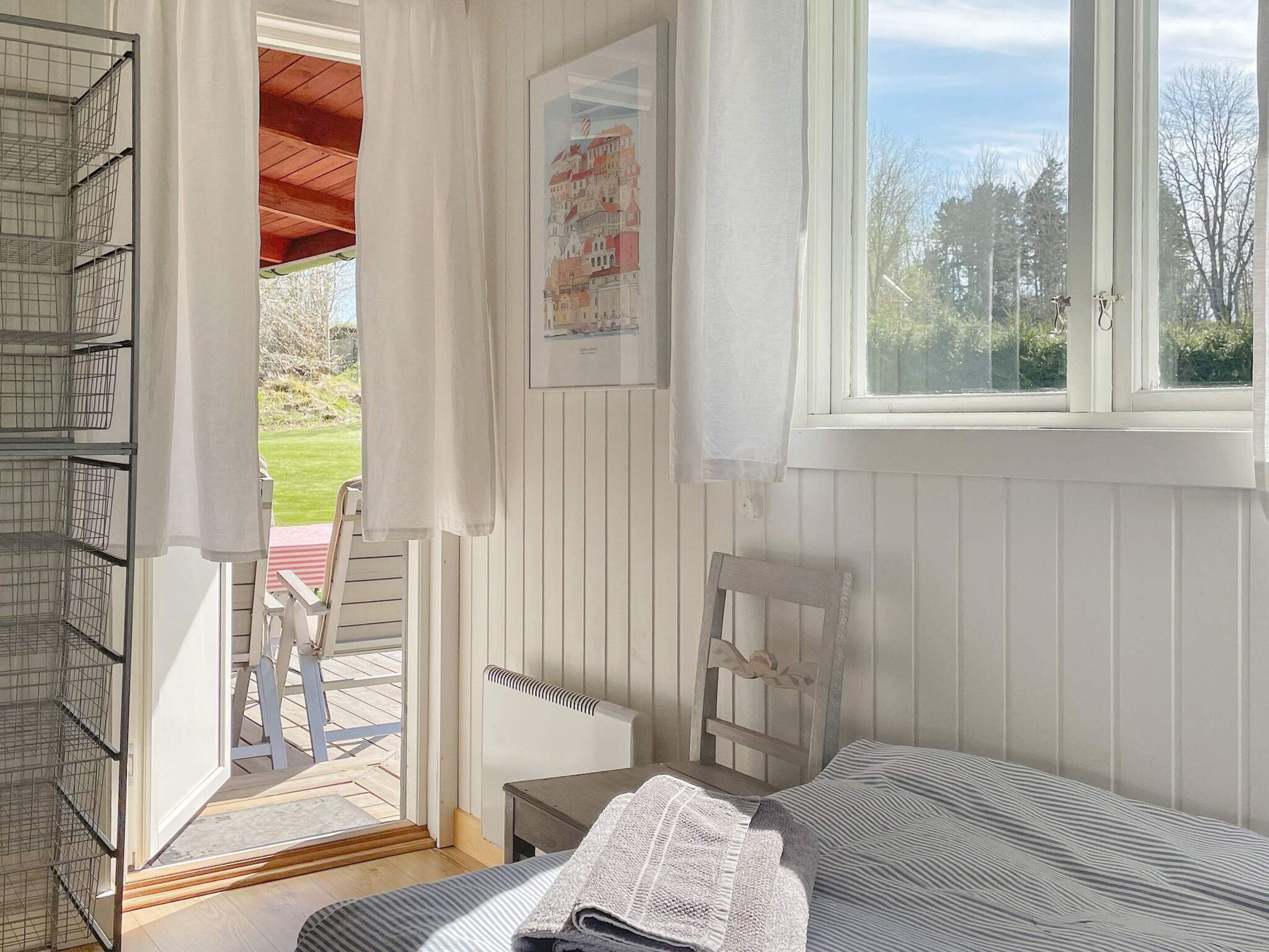 Una habitación con cama, una silla, un ventanal y una puerta que da a un espacio exterior.