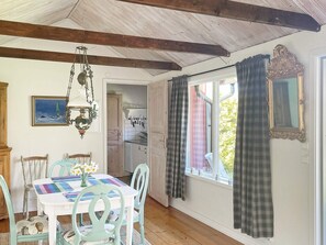 A dining area with a table set for four, chairs, a hanging light fixture, and a view of the kitchen through an open door.