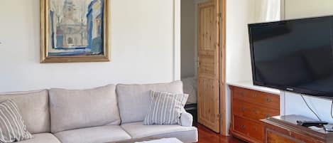 A living room with a sofa, a television, a wooden cabinet, and a painting on the wall.