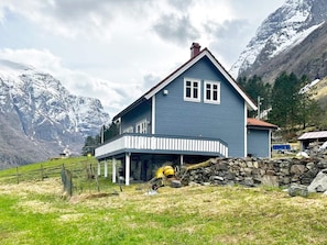A two-story house with a balcony, surrounded by mountains and a stone wall. - 6 Person Holiday Home in Gudvangen (Aurland)