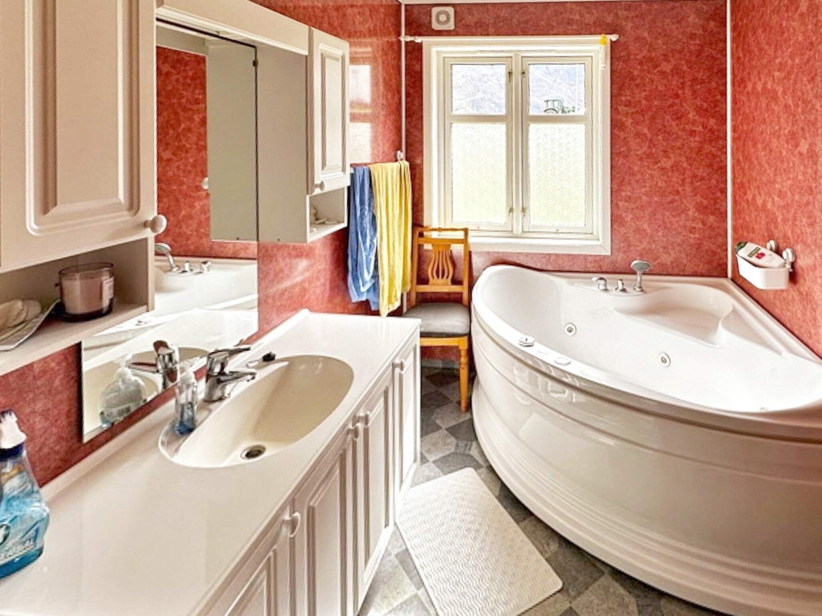 Une salle de bain avec une grande baignoire, un lavabo, un miroir et une fenêtre avec des rideaux.