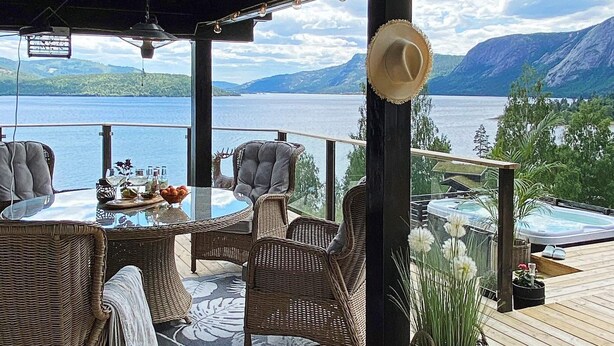A deck with wicker furniture, a glass table, and a view of a lake and mountains. - 10 Person Holiday Home in Treungen-by Traum (Nissedal)