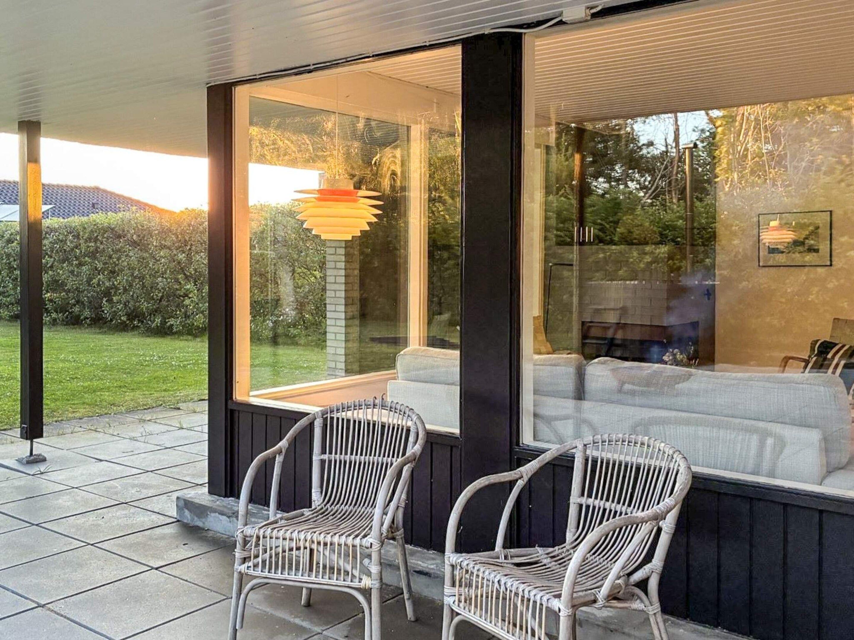 Una habitación con un ventanal grande, dos sillas de mimbre y vistas a un jardín.