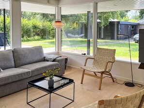 Un salon moderne avec un canapé gris, une chaise en bois et une table basse ornée d’un vase de fleurs.