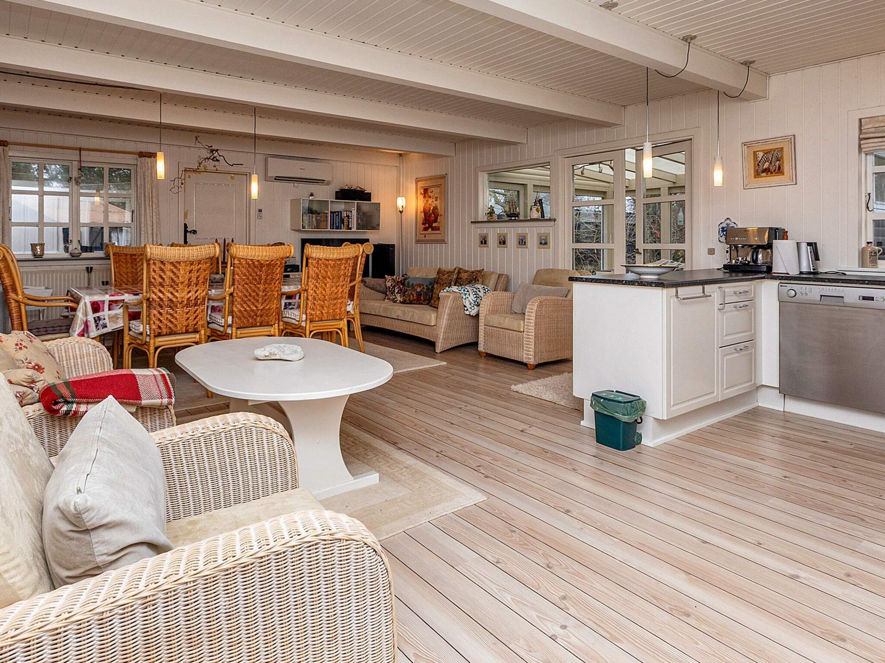 A spacious living area with wicker furniture, a white dining table, and a kitchen with white cabinets.