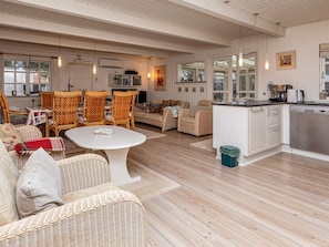 A spacious living area with wicker furniture, a white dining table, and a kitchen with white cabinets.