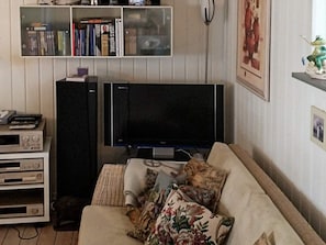 A living room with a flat-screen TV, a bookshelf, a sofa with floral cushions, and a small cabinet with electronic devices.
