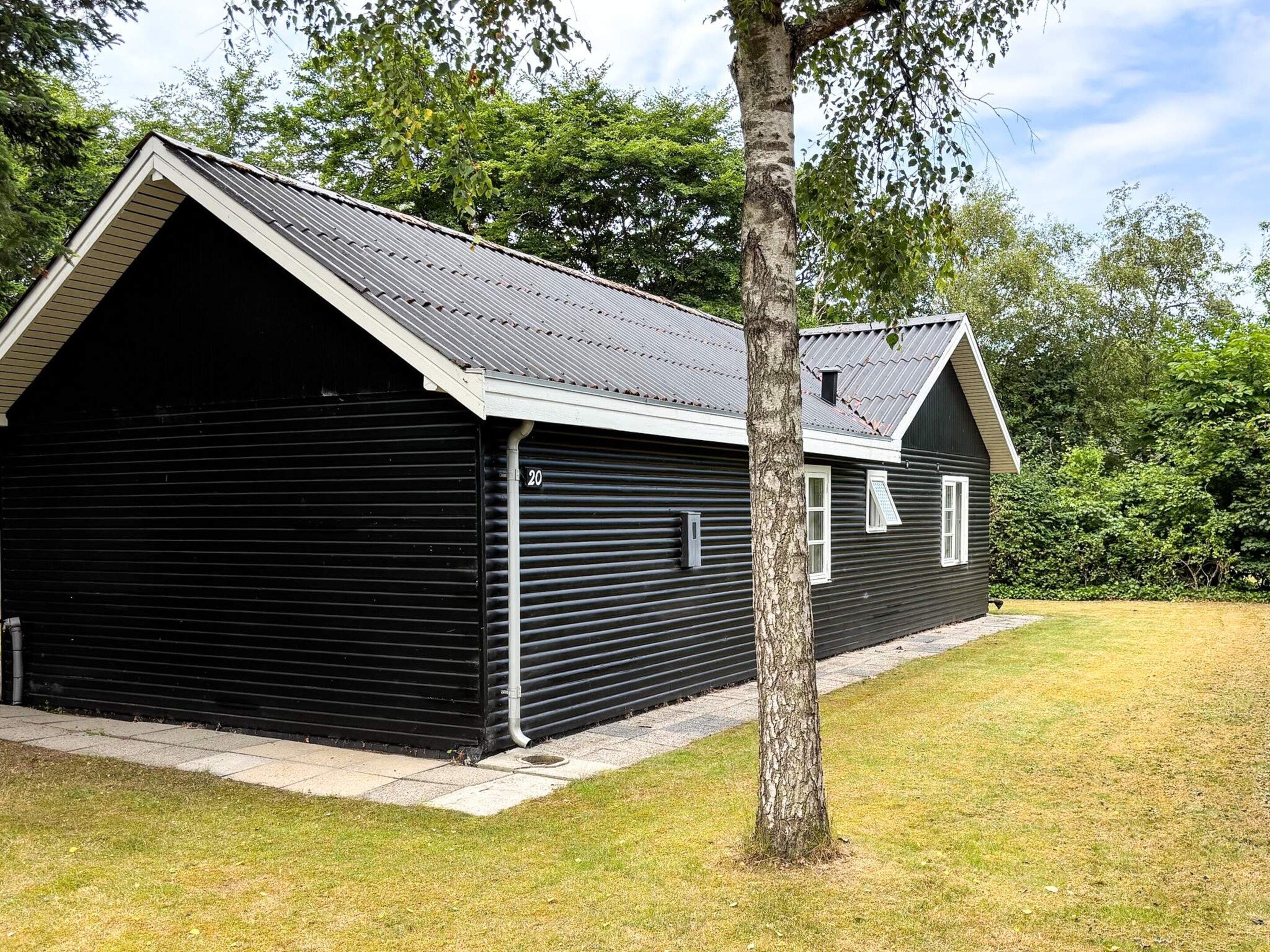 A black metal building with a sloped roof, a garage door, and a tree in front.