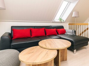 Un moderno apartamento tipo loft con un sofá de cuero negro, cojines rojos y dos mesitas de madera.