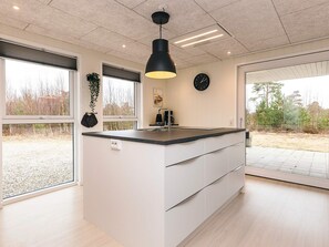 Una cocina moderna con una isla central, lámparas colgantes negras, un reloj en la pared y ventanas amplias.