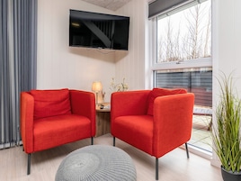 Uma sala de estar moderna com dois poltronas vermelhas, uma TV de tela plana, um abajur e uma planta em vaso.
