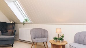Et moderne loftværelse med skråvægge, en grå sofa, to lænestole, et træsidebord med planter og en radiator.