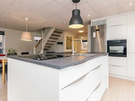 Cozinha moderna com ilha central, eletrodomésticos de aço inoxidável e escada para um andar superior.