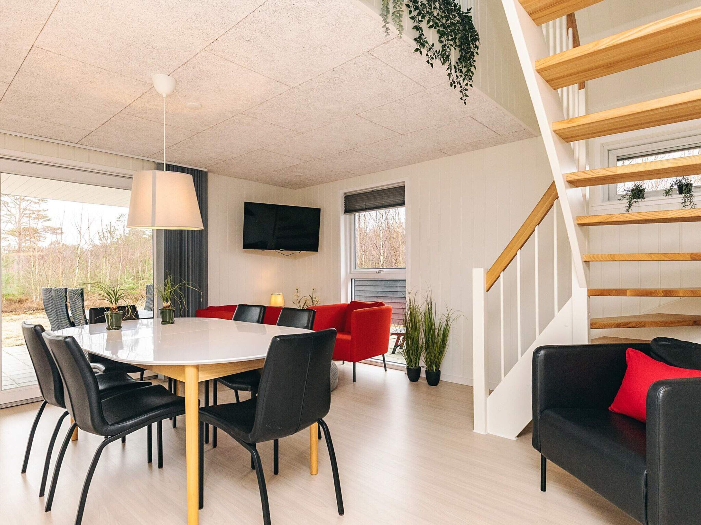 A modern interior with a dining table, chairs, a red sofa, a staircase, and a TV mounted on the wall.