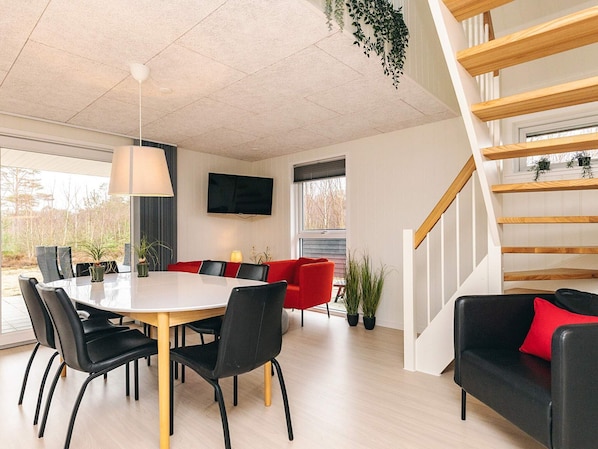 Un interior moderno con una mesa de comedor, sillas, un sofá rojo, una escalera y un televisor montado en la pared.