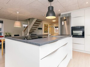 Eine moderne Küche mit einer zentralen Kochinsel, Edelstahlgeräten und einer Treppe, die zu einer anderen Ebene führt.