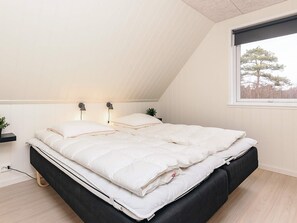 A bedroom with a sloped ceiling, a bed with a black frame, white bedding, and two bedside lamps.