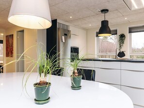 A modern kitchen with white cabinets, a white countertop, and two potted plants.