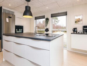 Eine moderne Küche mit einer zentralen Kochinsel, einem Einbauofen, einem Kühlschrank und einer hängenden Pflanze.
