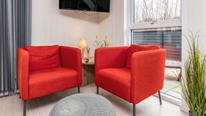 En moderne stue med to røde lænestole, et fladskærms-tv, et lille sofabord med en lampe og en potteplante.