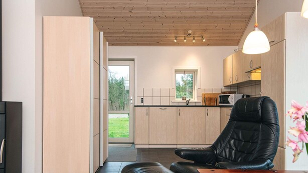 A modern kitchen with wooden cabinets, a black leather chair, and a dining table. - 5 Person Holiday Home in Bording (Bording)