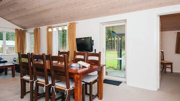 Comedor con mesa y sillas de madera, televisor y ventanas grandes con cortinas.