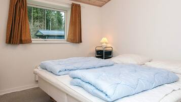 Un dormitorio con dos camas, una ventana con cortinas, una lámpara de noche y vista a una casa afuera.