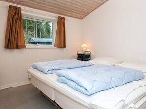 A bedroom with two beds, a window with curtains, a bedside lamp, and a view of a house outside.