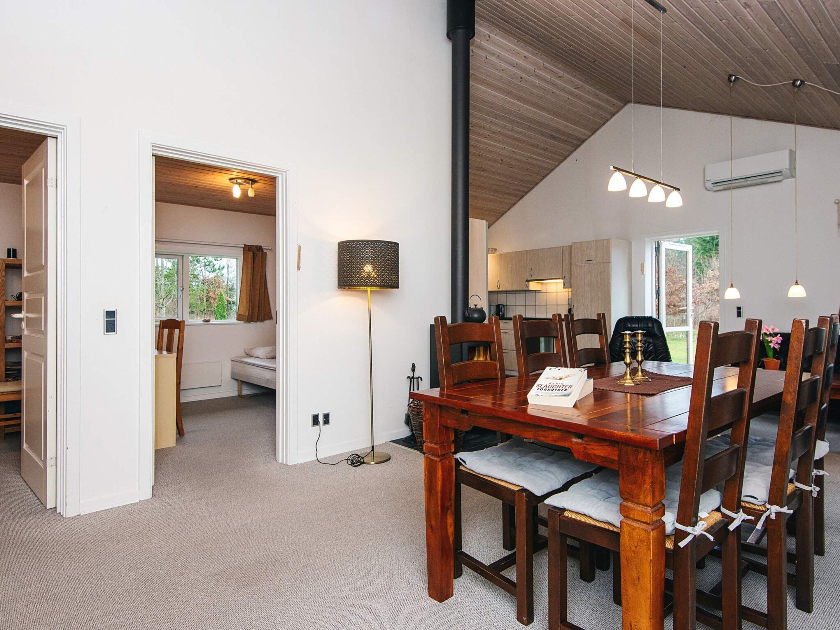A dining area with a wooden table and chairs, a floor lamp, and a view into the kitchen.