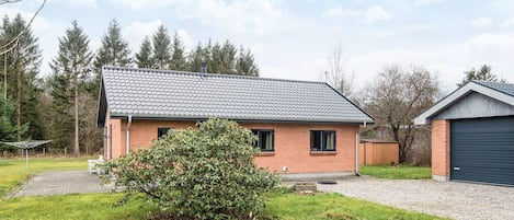 A single-story house with a tiled roof, a brick exterior, and a small front yard with a bush.