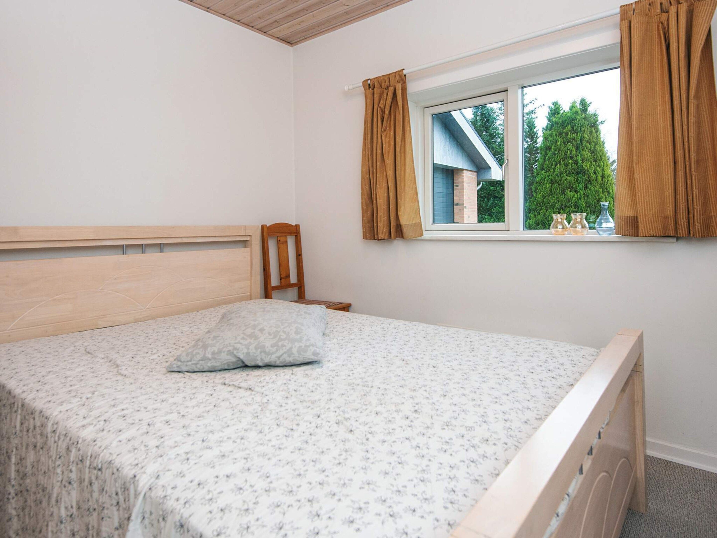 Une chambre avec un cadre de lit en bois, un lit simple, une fenêtre avec des rideaux et une vue sur la verdure à l’extérieur.