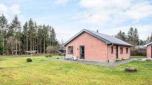 A single-story brick house with a sloped roof, a front porch with a bench, and a small garden area with a lawn and trees in the background. - 5 Person Holiday Home in Bording (Bording)