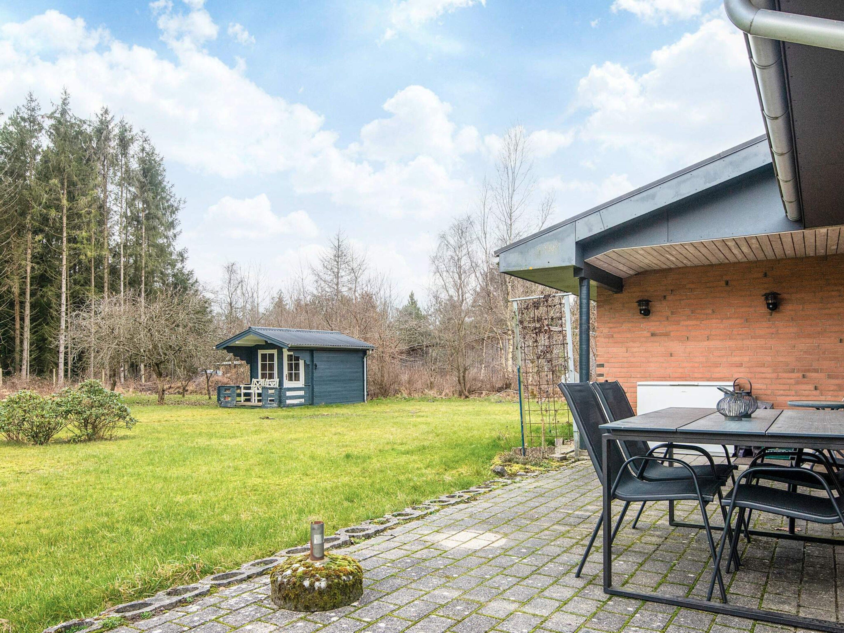 A patio area with a table and chairs, a small shed, and a brick building in the background.