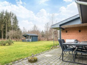 A patio area with a table and chairs, a small shed, and a brick building in the background.