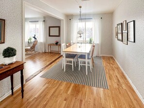 A dining room with a wooden table and chairs, a rug, and a potted plant.